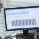 Woman smiling at camera with data on computer in the background